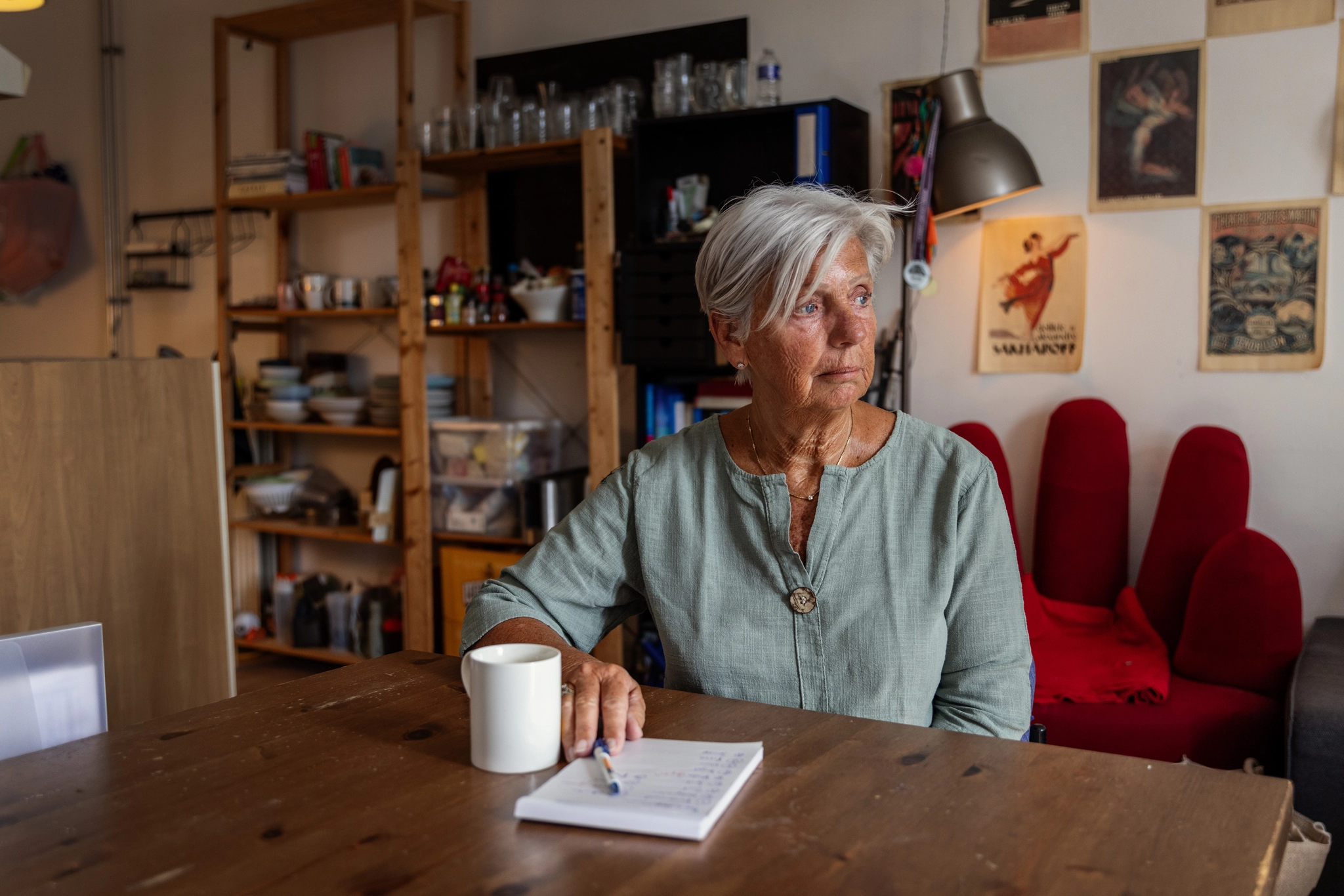 Grijsharige vrouw aan houten tafel met notitieboekje en koffie, nadenkend over haar werk in het sociaal domein