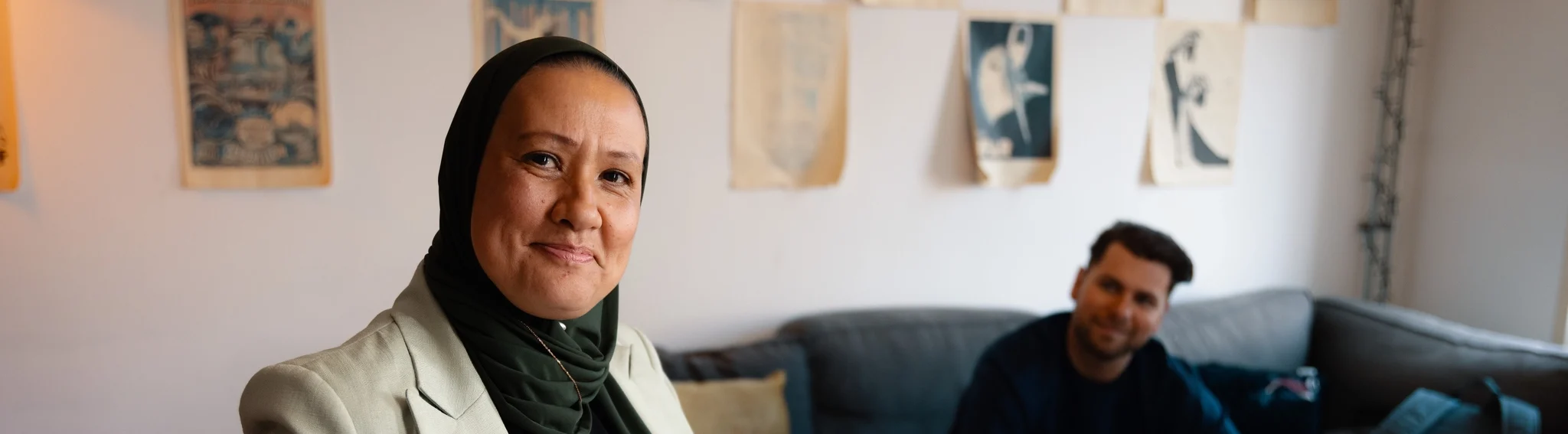 Professional in hijab glimlacht zelfverzekerd in een ruimte met kunst aan de muur, collega op de achtergrond
