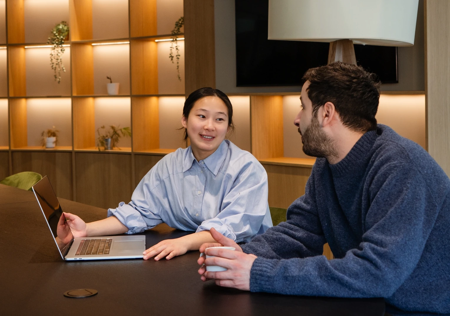 Twee collega's bespreken een opleiding sociaal domein aan tafel met een laptop in een moderne vergaderruimte