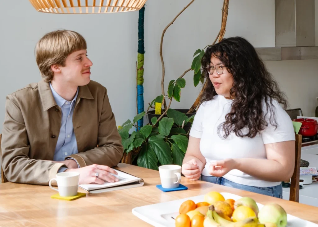 Twee professionals bespreken opleidingen sociaal domein aan een keukentafel met koffie en een notitieboek