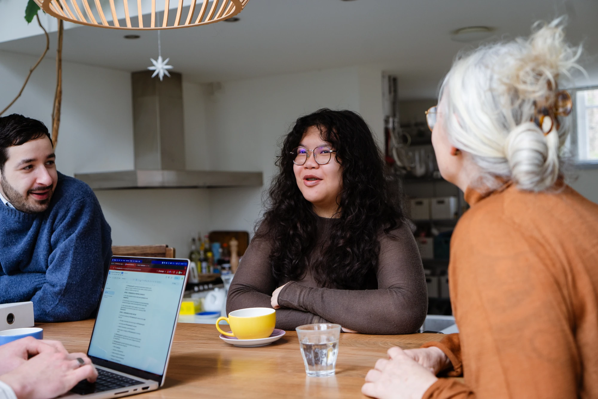Drie professionals aan tafel in gesprek tijdens een PEX Academy opleiding in het sociaal domein, met laptop en koffie