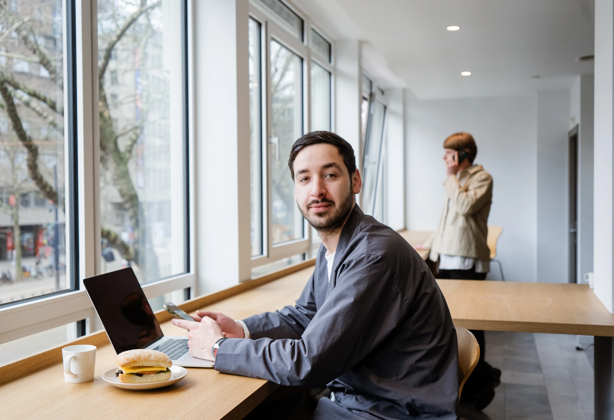 Man werkt aan laptop met sandwich en koffie in modern studieruimte tijdens PEX Academy opleiding sociaal domein